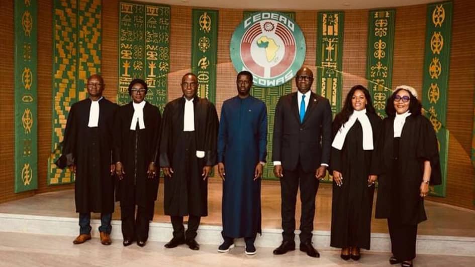 Five newly sworn-in ECOWAS Court judges in judicial robes standing with officials in front of the ECOWAS emblem