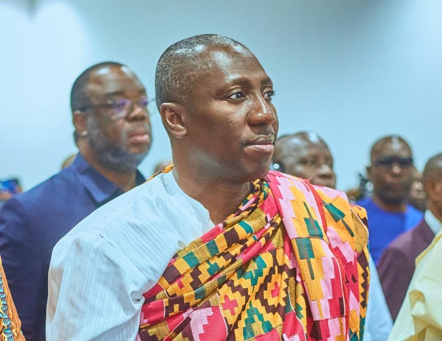 A man in traditional kente cloth standing among a group of officials