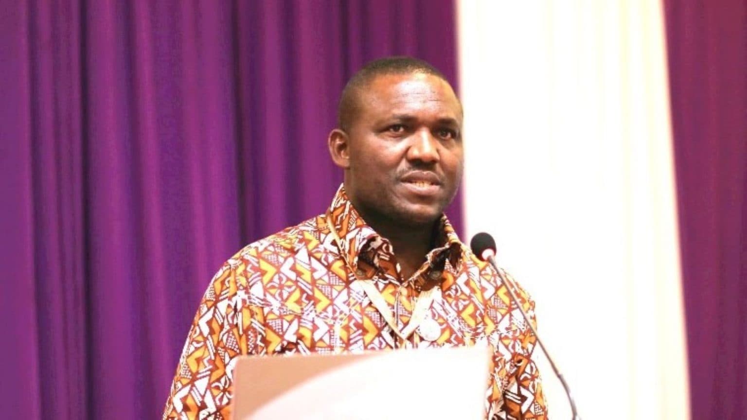 A man in a patterned shirt speaking at a podium microphone