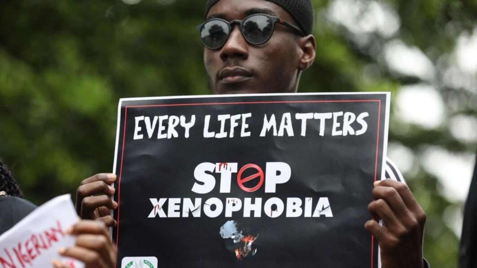 A protester holding a sign reading 'Every Life Matters, Stop Xenophobia' at a demonstration