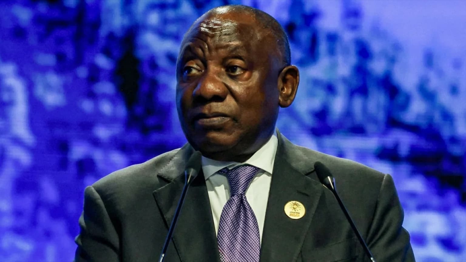South African President Cyril Ramaphosa speaking at a podium against a blue backdrop