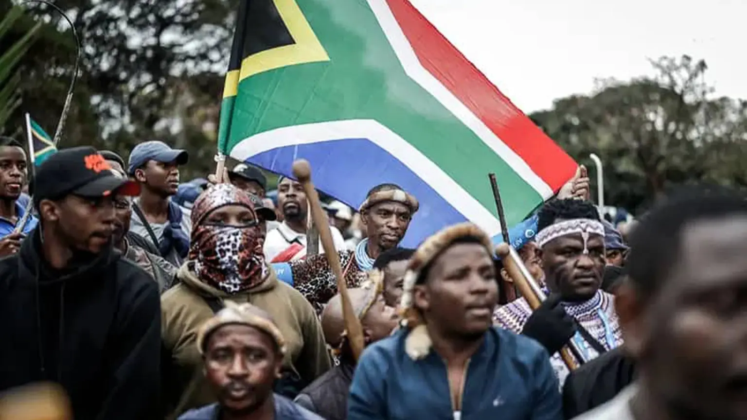 A crowd of demonstrators in South Africa holding a large South African flag
